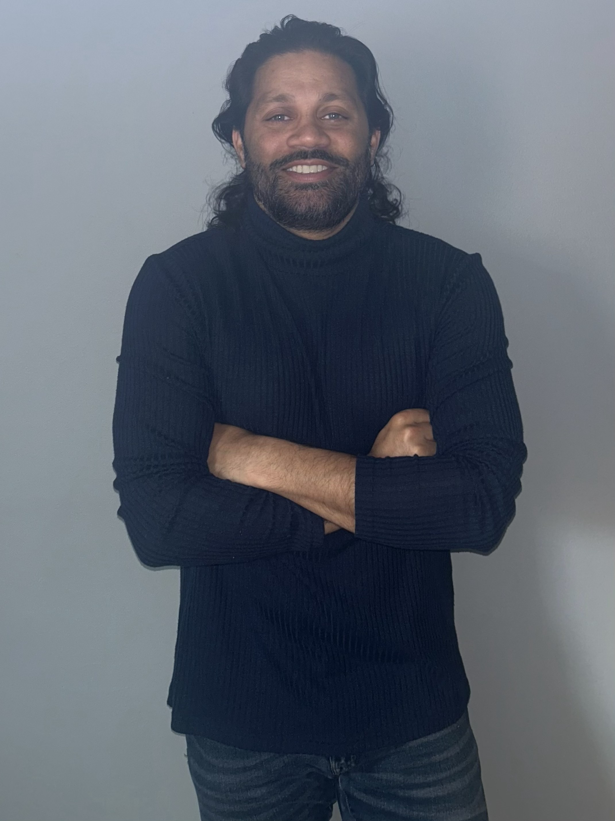 Alexander Mathai - Professional headshot with arms crossed in navy turtleneck